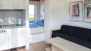 A compact kitchen with a stove, a sink, and a window. There is a dark sofa and a small table in the living area. - Beautiful studio in Løgumkloster (Løgumkloster)