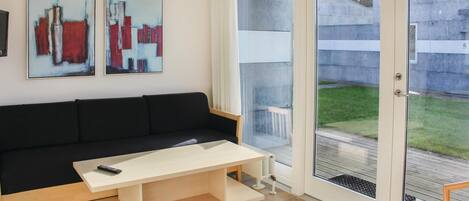 A modern living room with a black sofa, a light wooden coffee table, and two abstract paintings on the wall.