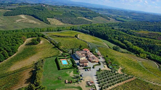 Vue aérienne d’un domaine viticole avec des terrasses cultivées, une piscine et un bâtiment principal entouré de voitures garées.