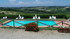 Un espace piscine avec des chaises longues blanches et une vue sur des collines verdoyantes en arrière-plan.