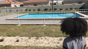 En swimmingpool omgivet af et hvidt hegn, med bygninger og bjerge i baggrunden.