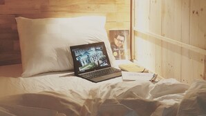 A bed with a laptop, a pillow, a notebook, and a poster on a wooden wall. - KHA Hostel & Cafe (Ho Chi Minh City)