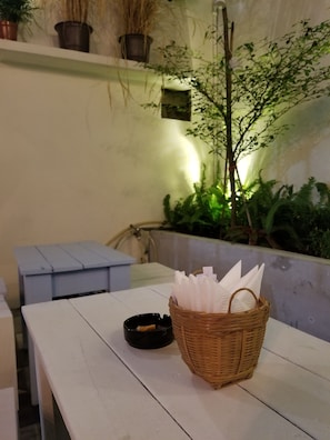 A table with a wicker basket containing napkins and a black ashtray with a cigarette butt.