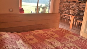 A bedroom with a large bed, a stone fireplace, and a view of a grassy field through a window. - Alcove du Velay (Polignac)