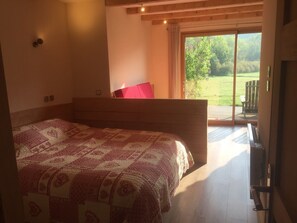 A bedroom with a large bed, a wooden headboard, a red pillow, and a sliding glass door leading to a balcony with a view of greenery. - Alcove du Velay (Polignac)