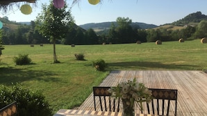 An outdoor seating area with a wooden deck, a table with chairs, and a vase of flowers. - Alcove du Velay (Polignac)