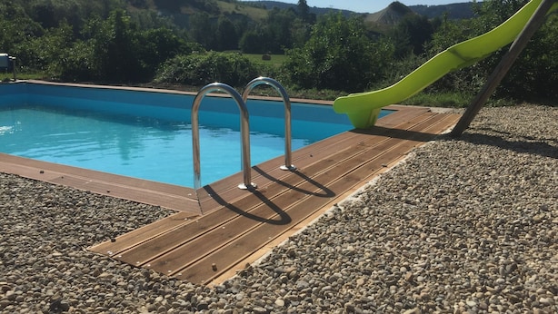 A swimming pool with a wooden deck and metal pool ladder. - Alcove du Velay (Polignac)
