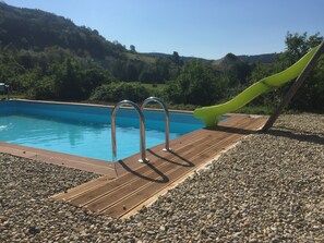 A swimming pool with a wooden deck and metal pool ladder. - Alcove du Velay (Polignac)