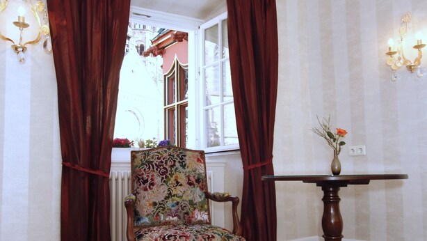 A room with a patterned armchair, a small table with a vase, and curtains. - Hotel Oberkirch (Freiburg)