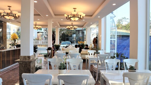Un espacio interior amplio con varias mesas y sillas, ventanas grandes y candelabros decorativos.