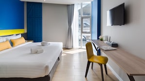 Habitación de hotel con cama, escritorio, silla, televisor de pantalla plana y ventana con vistas al exterior.