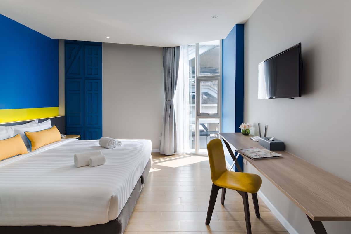 A hotel room with a bed, a desk, a chair, a TV, and a window.