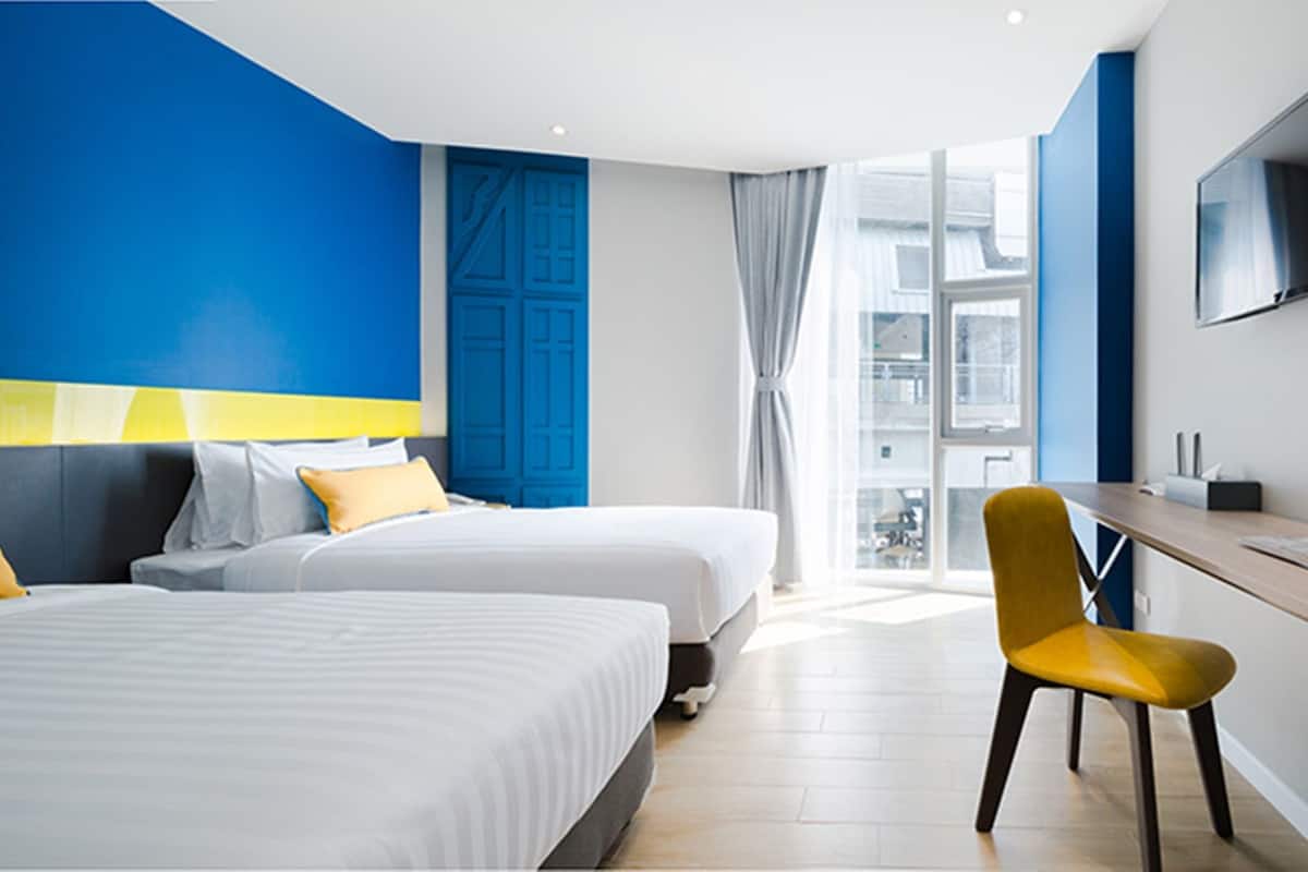 A hotel room with two beds, a desk, a chair, a TV, and a view of the city.