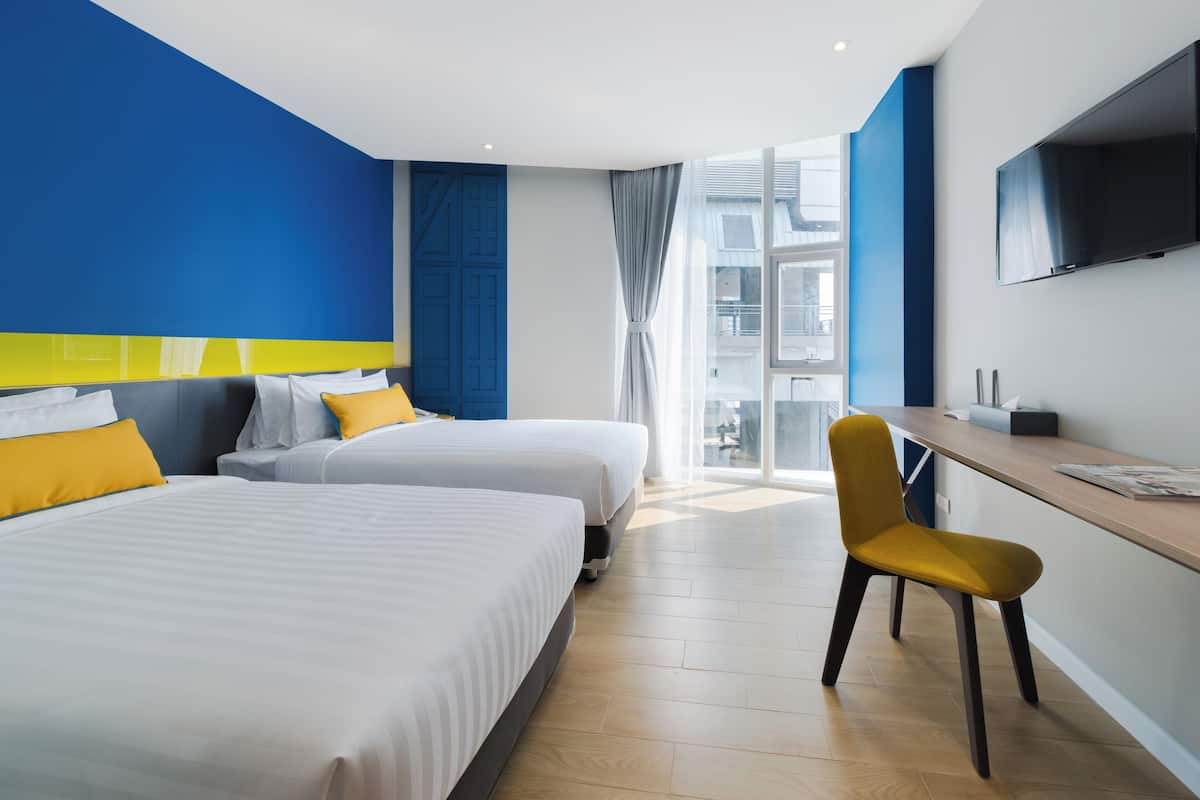 A hotel room with two beds, a desk, a chair, a TV, and a large window.