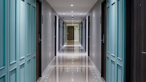 Un pasillo largo y estrecho con puertas color turquesa a ambos lados, que conduce a una habitación al final.