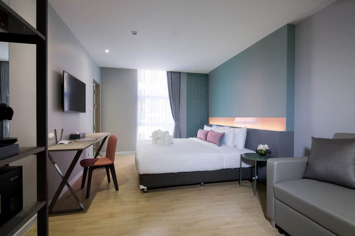 A modern hotel room with a bed, desk, and seating area.