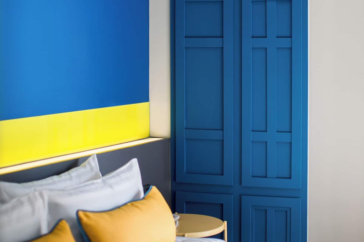 A bedroom with a bed, pillows, a round table, and a blue wall with a geometric design.