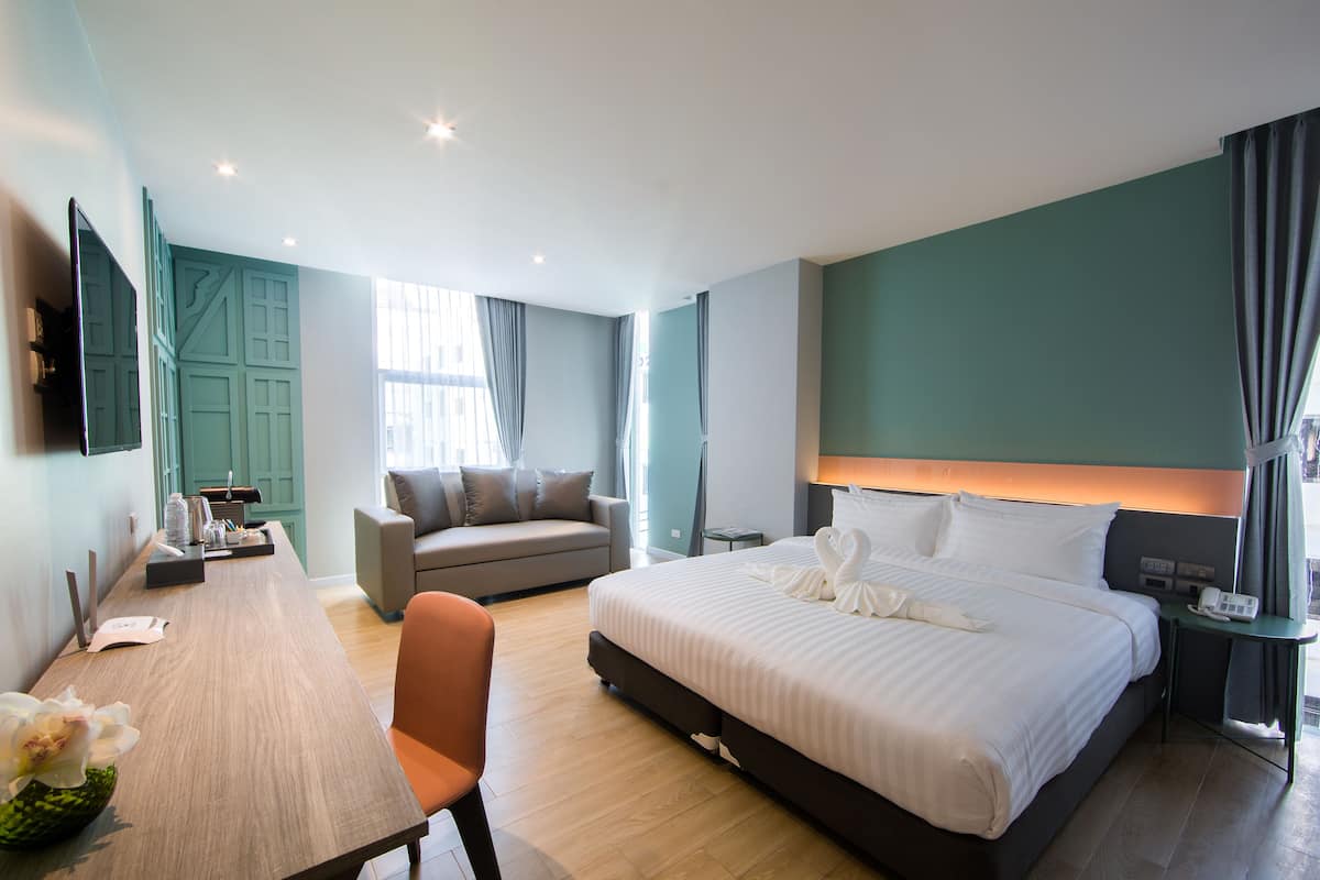 A hotel room with a bed, a desk, a sofa, a TV, and a window with curtains.