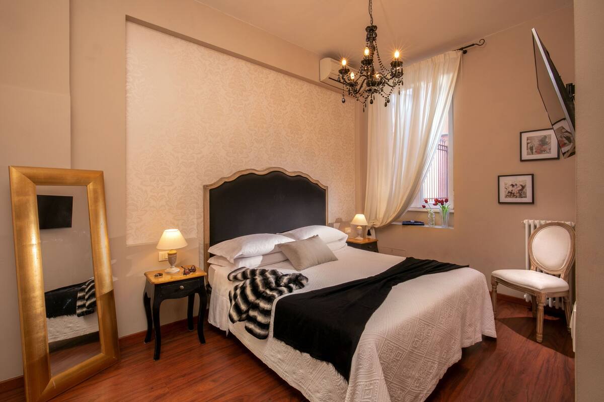 A neatly arranged bedroom with a large bed, bedside tables, a mirror, and a chandelier.