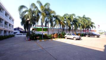 Un estacionamiento con varios coches, palmeras y un edificio con balcones.