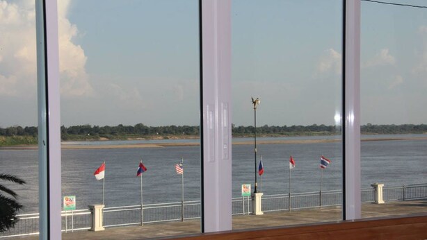 A view from a window overlooking a waterfront with flags and a lamp post. - Thatphanom River View Hotel (That Phanom)