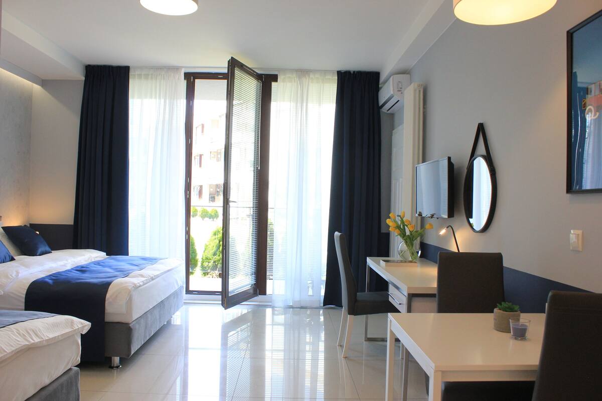 A hotel room with a bed, a desk, a chair, a TV, and a window with curtains.