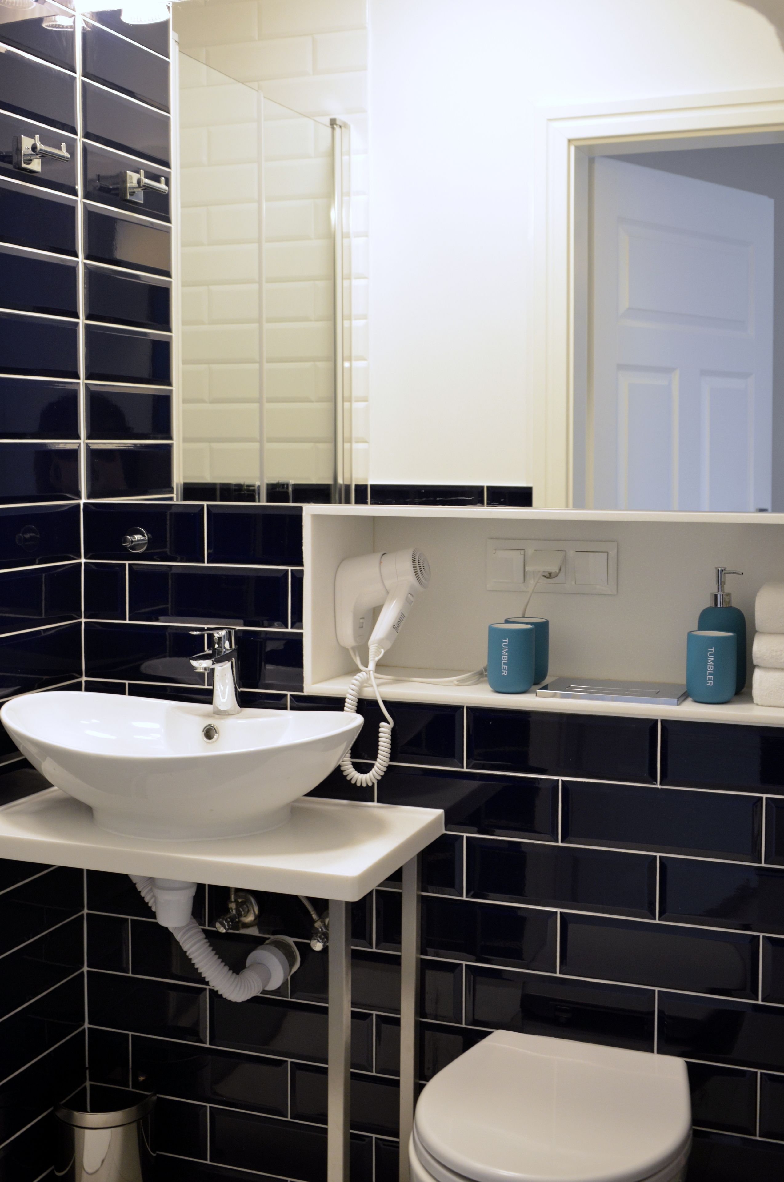 A modern bathroom with a white sink, a toilet, and a mirror above the sink. There are two blue containers on the sink's edge and a white towel hanging on the wall.