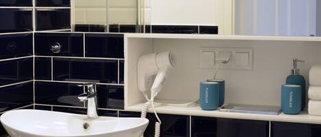 A modern bathroom with a white sink, a toilet, and a mirror above the sink. There are two blue containers on the sink's edge and a white towel hanging on the wall.