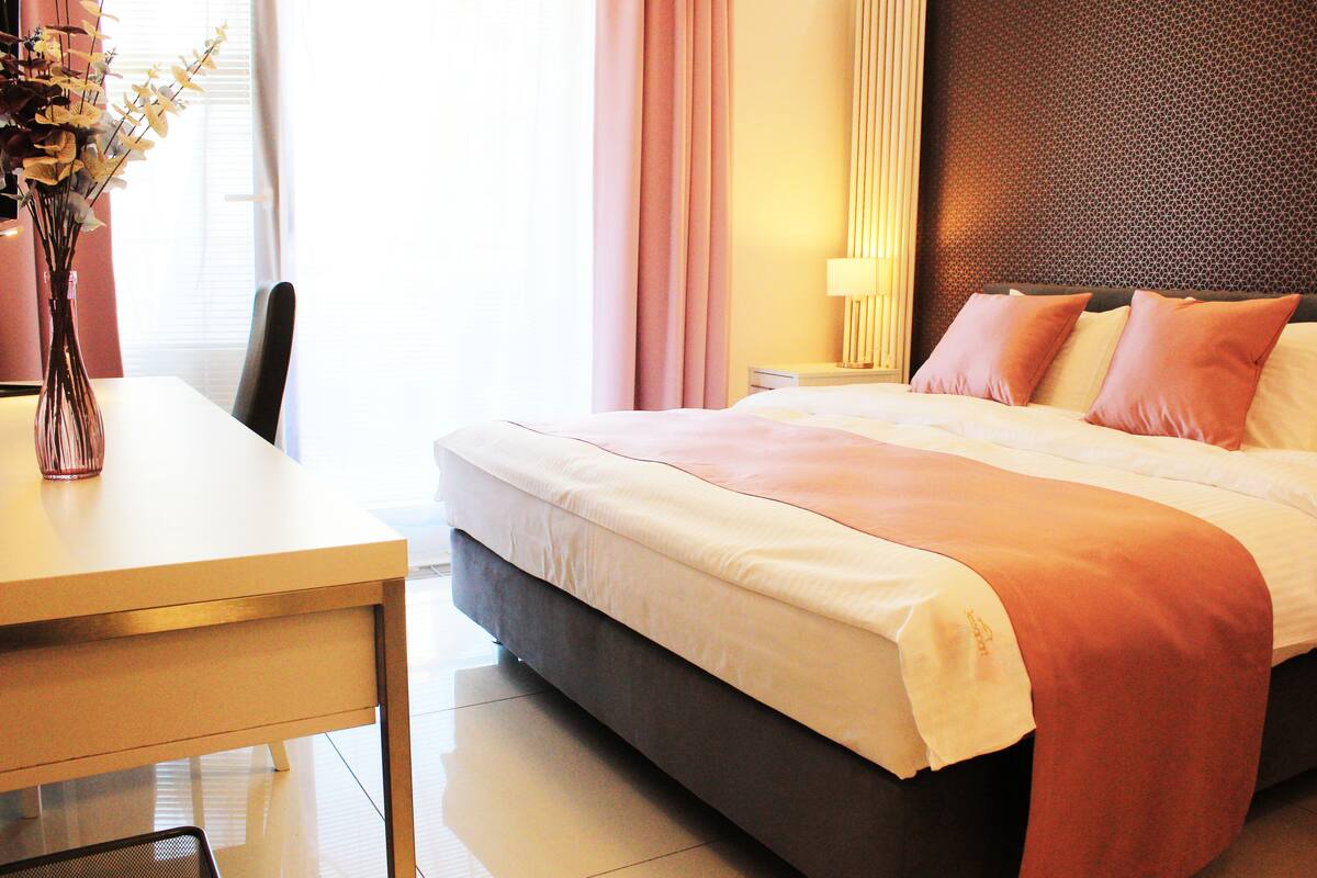 A hotel room with a bed, a desk, and a vase of flowers.
