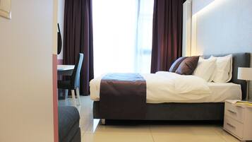 A hotel room with a bed, bedside table, chair, and a view of the outside through the window.
