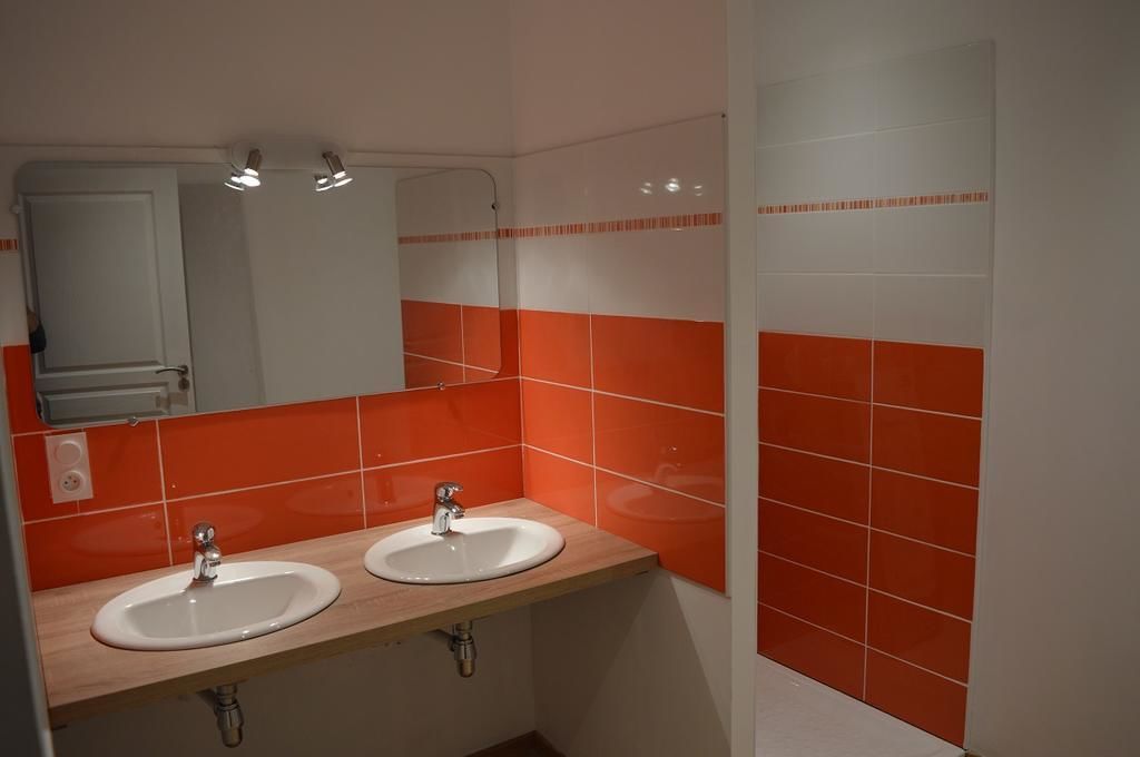 Uma casa de banho com duas pias, um espelho e paredes azulejadas em laranja.