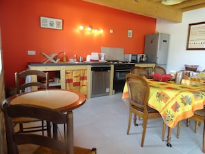 A kitchen with a dining area, featuring a wooden table, chairs, a refrigerator, and a microwave. - Ferme Passion (Saint-Trivier-sur-Moignans)
