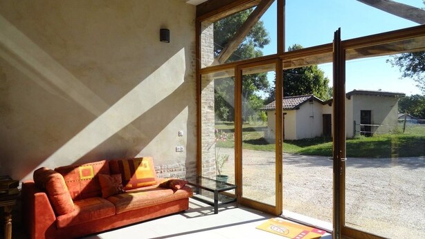Una habitación con un gran ventanal corredera que da a un camino de entrada, un sofá rojo y una pequeña mesa.