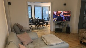 Un salon comprenant un canapé, une table basse en verre, un téléviseur et un coin repas avec des chaises et une table.