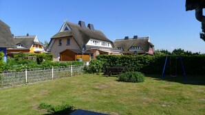 Un quartier résidentiel avec des maisons aux toits de chaume, une cour clôturée et un ensemble de jeux avec une balançoire.