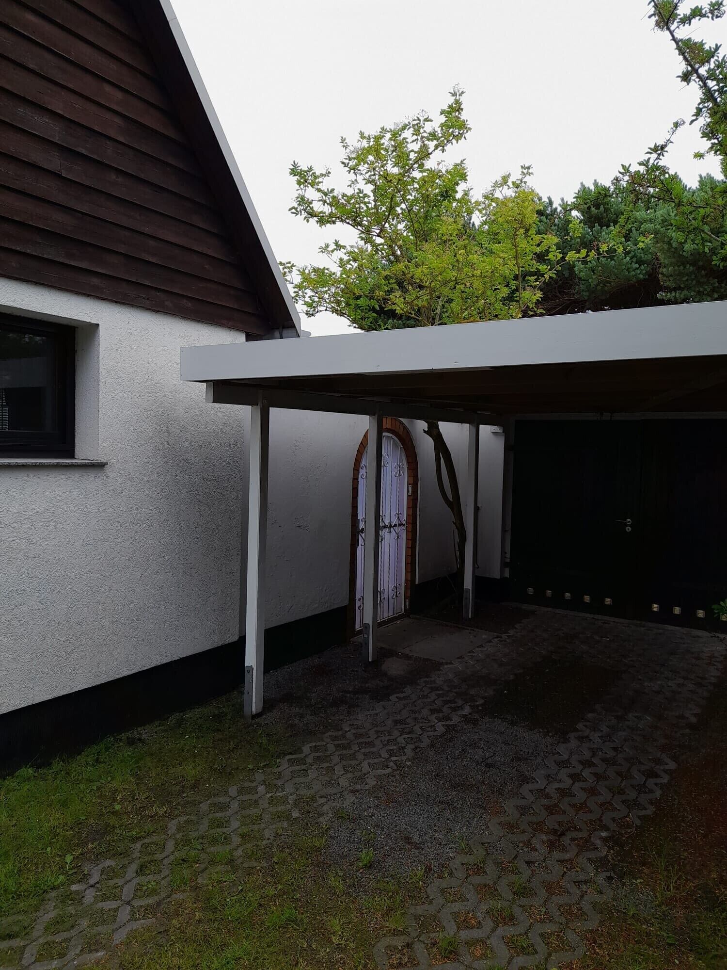 A covered driveway leading to a garage with a white wall and a window.