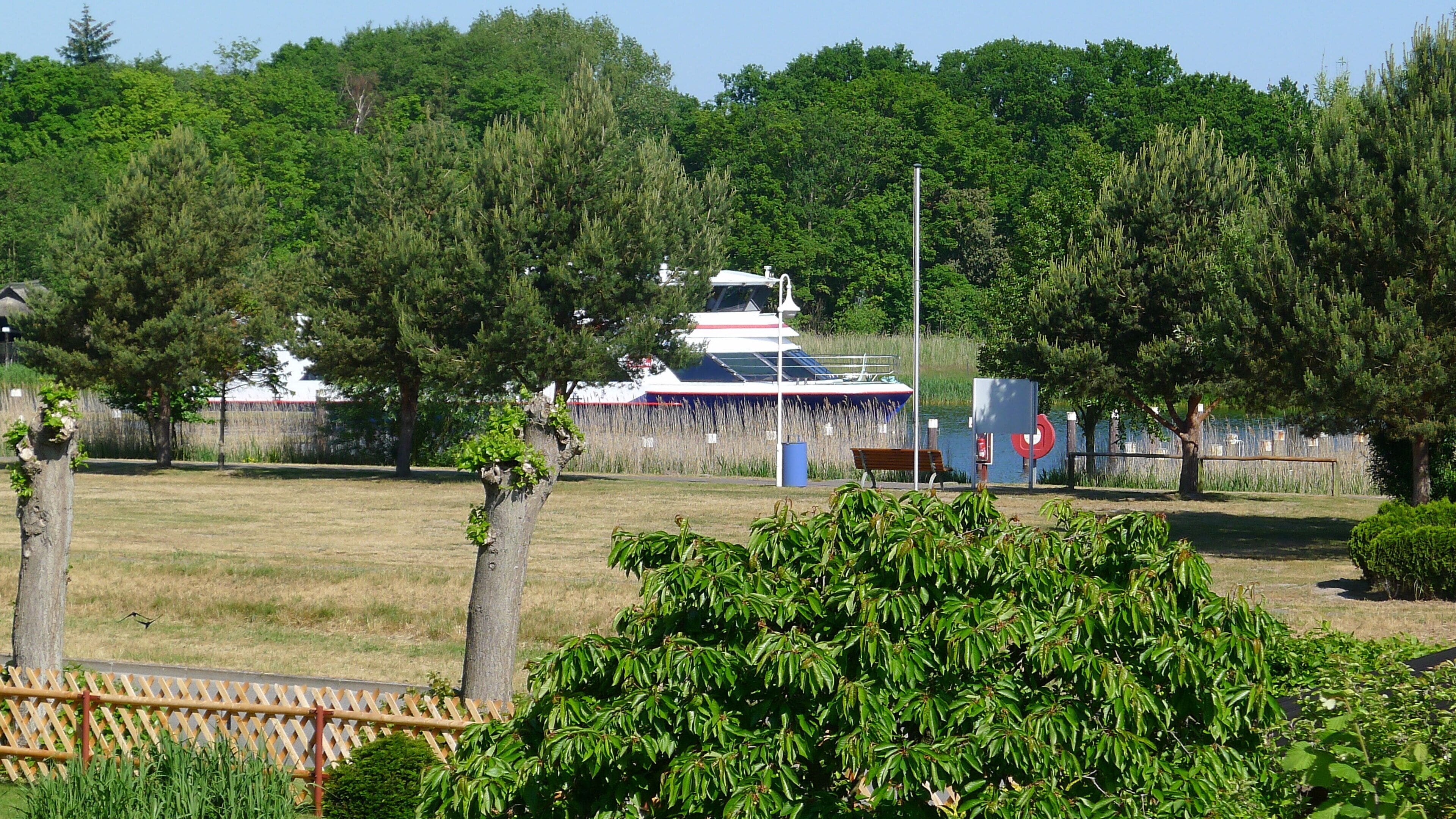 A boat docked near a grassy area with trees and a fence.