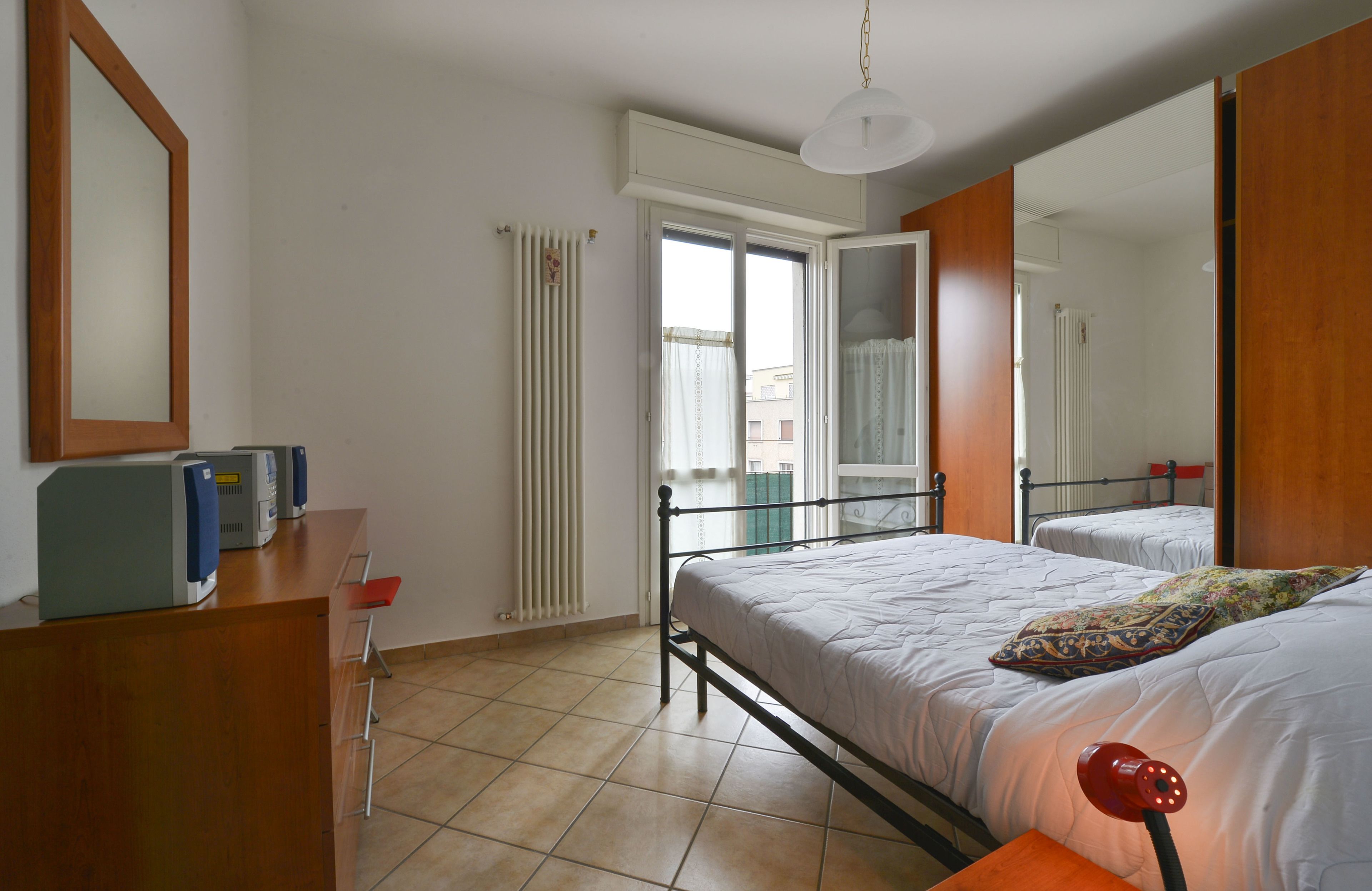A bedroom with a bed, a desk, a chair, a radiator, and a window.