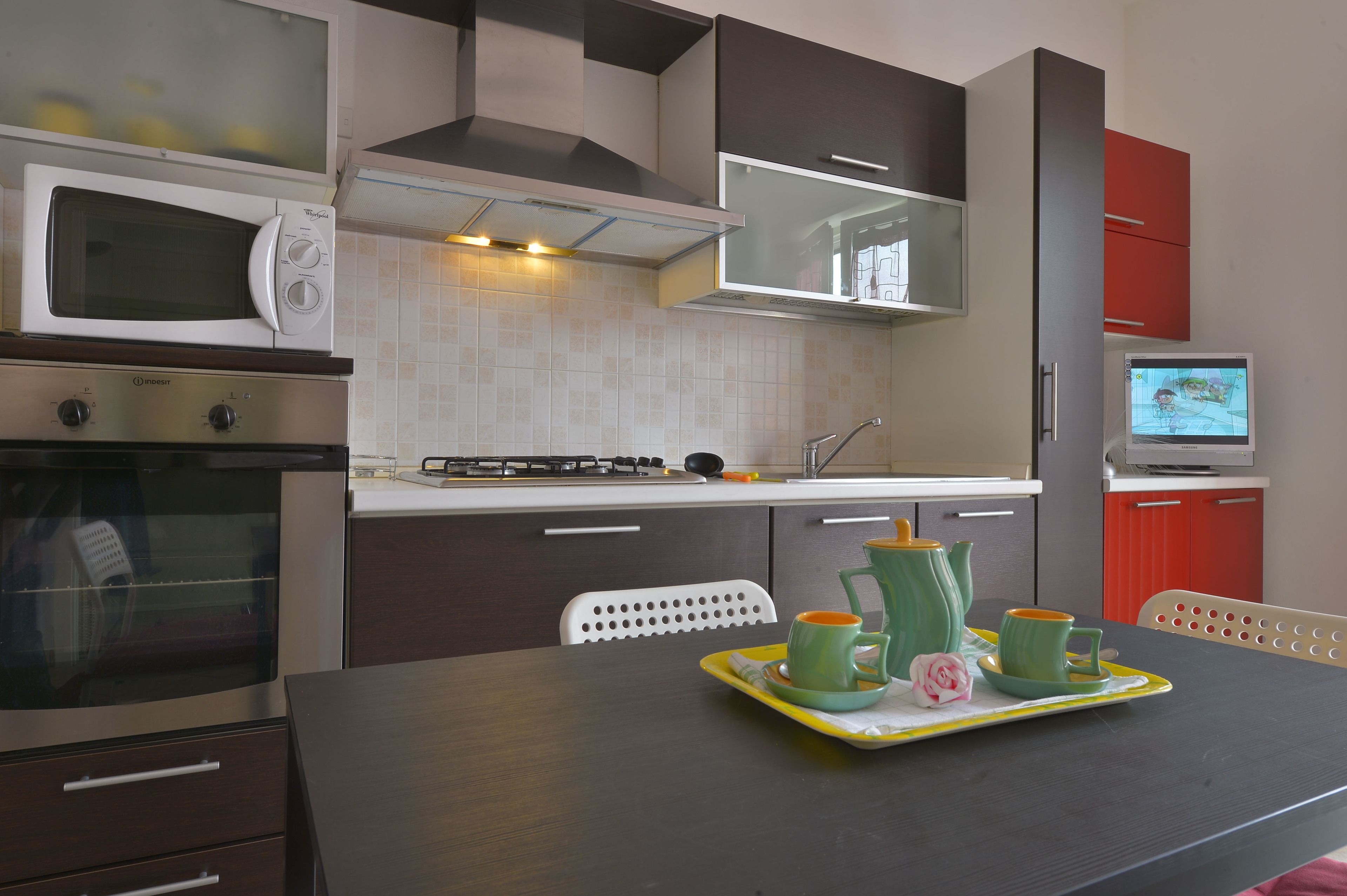 Una cocina moderna con microondas, horno y comedor, con una bandeja de tazas verdes y una rosa.