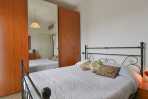 A bedroom with two beds, wooden wardrobe, and a mirror.
