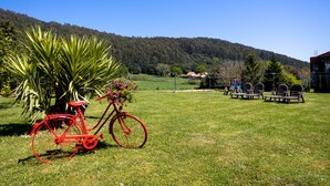 Una bicicleta roja con una cesta de flores, una palmera y un campo de césped con una montaña al fondo.