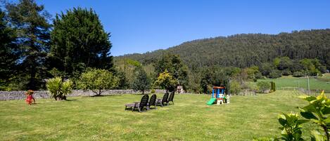 A grassy outdoor area with a play structure, a stone wall, and trees.