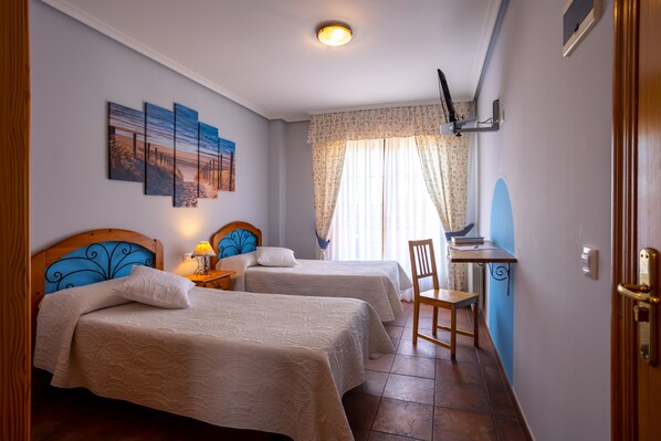 Una habitación de hotel con dos camas, un escritorio, una silla, una lámpara y un ventanal con cortinas.
