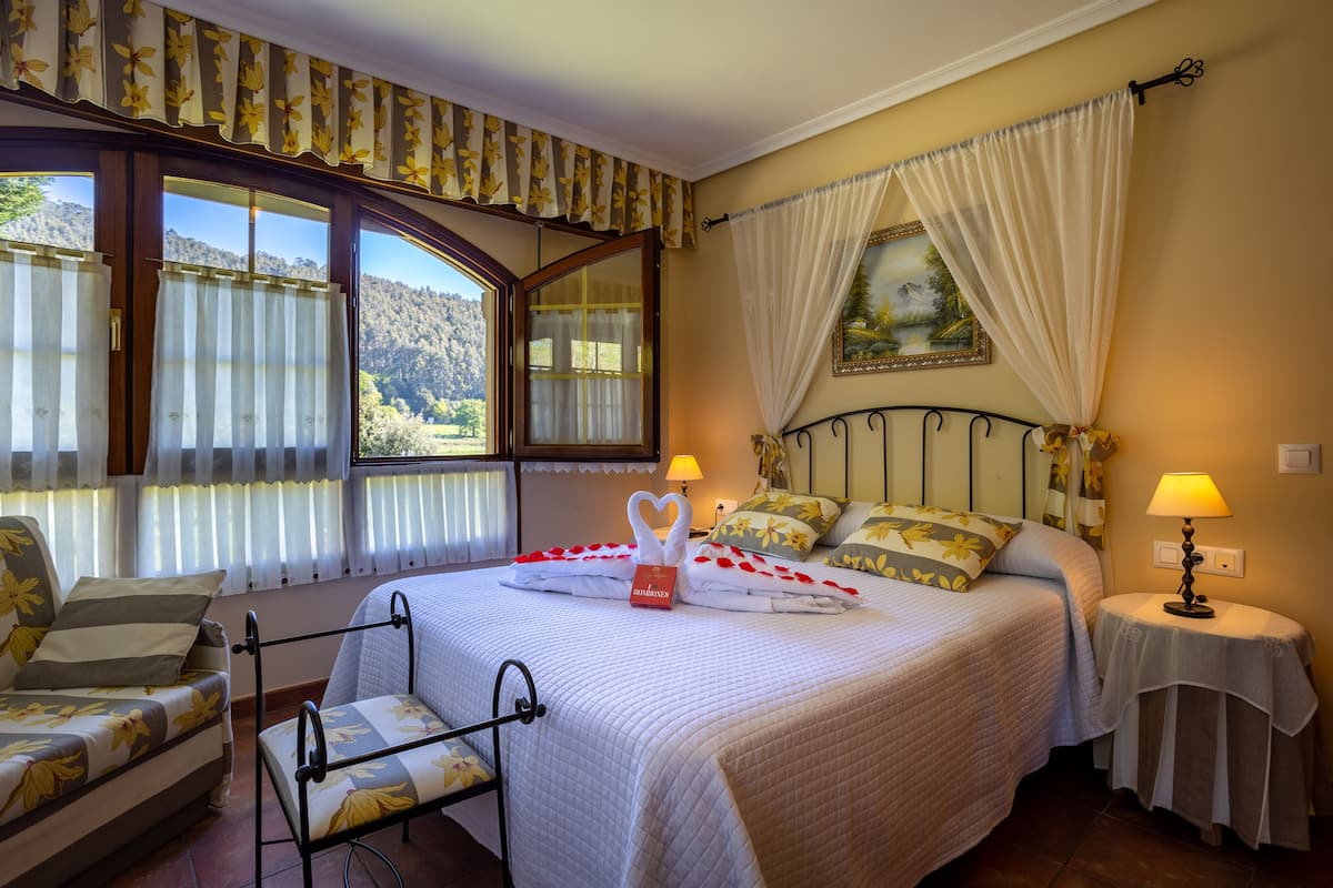A bedroom with a large bed, two bedside tables, a chair, and a window with curtains.