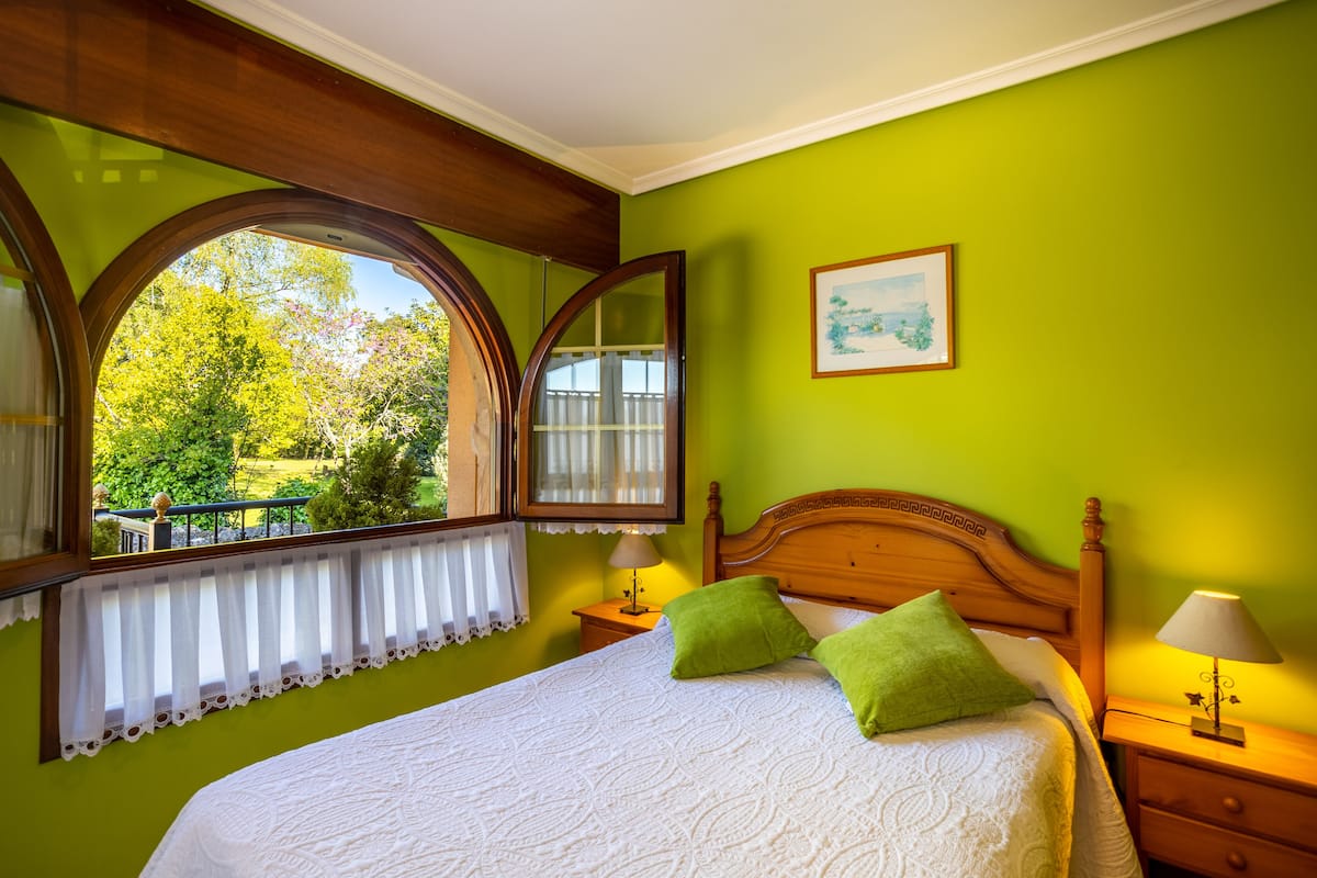 A bedroom with a large bed, green walls, a window with a view of trees, and a wooden headboard.