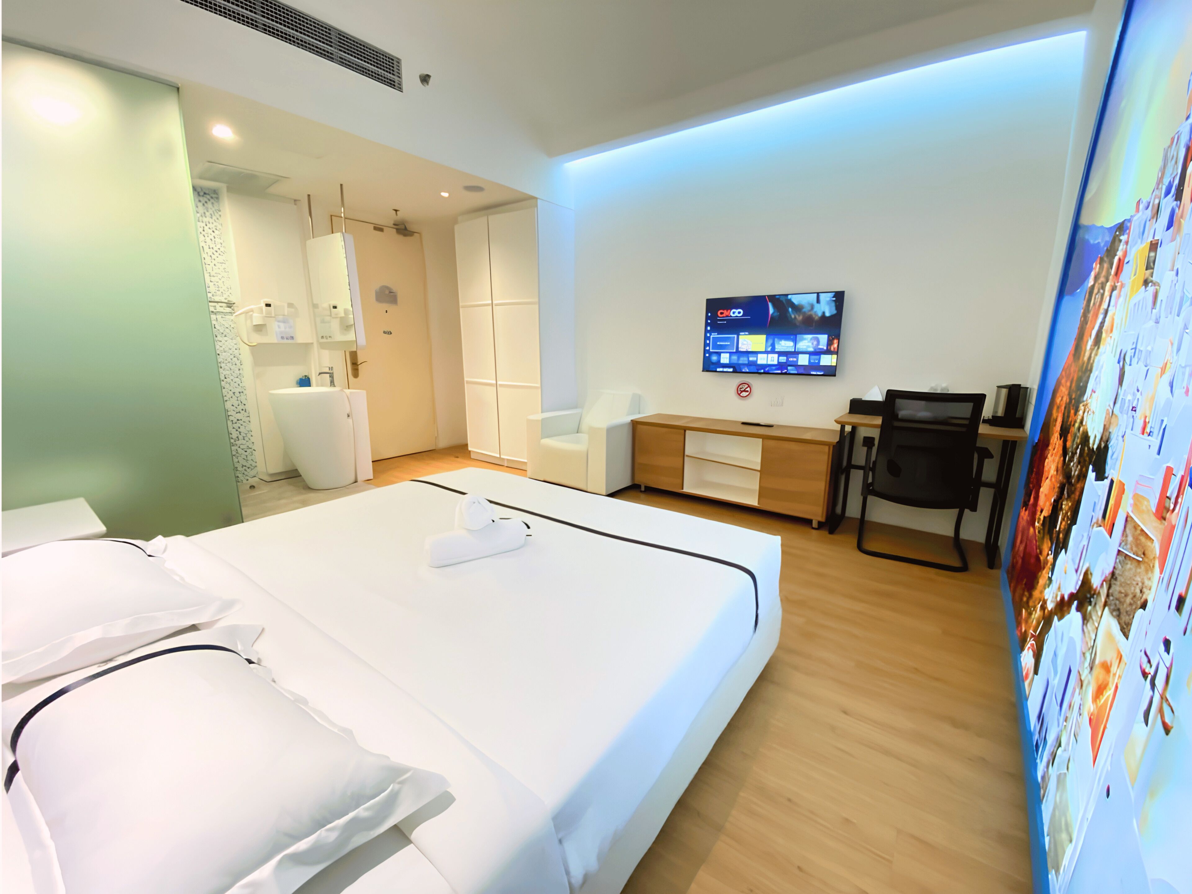 A hotel room with a bed, a desk, a chair, a television, and a wall-mounted artwork.