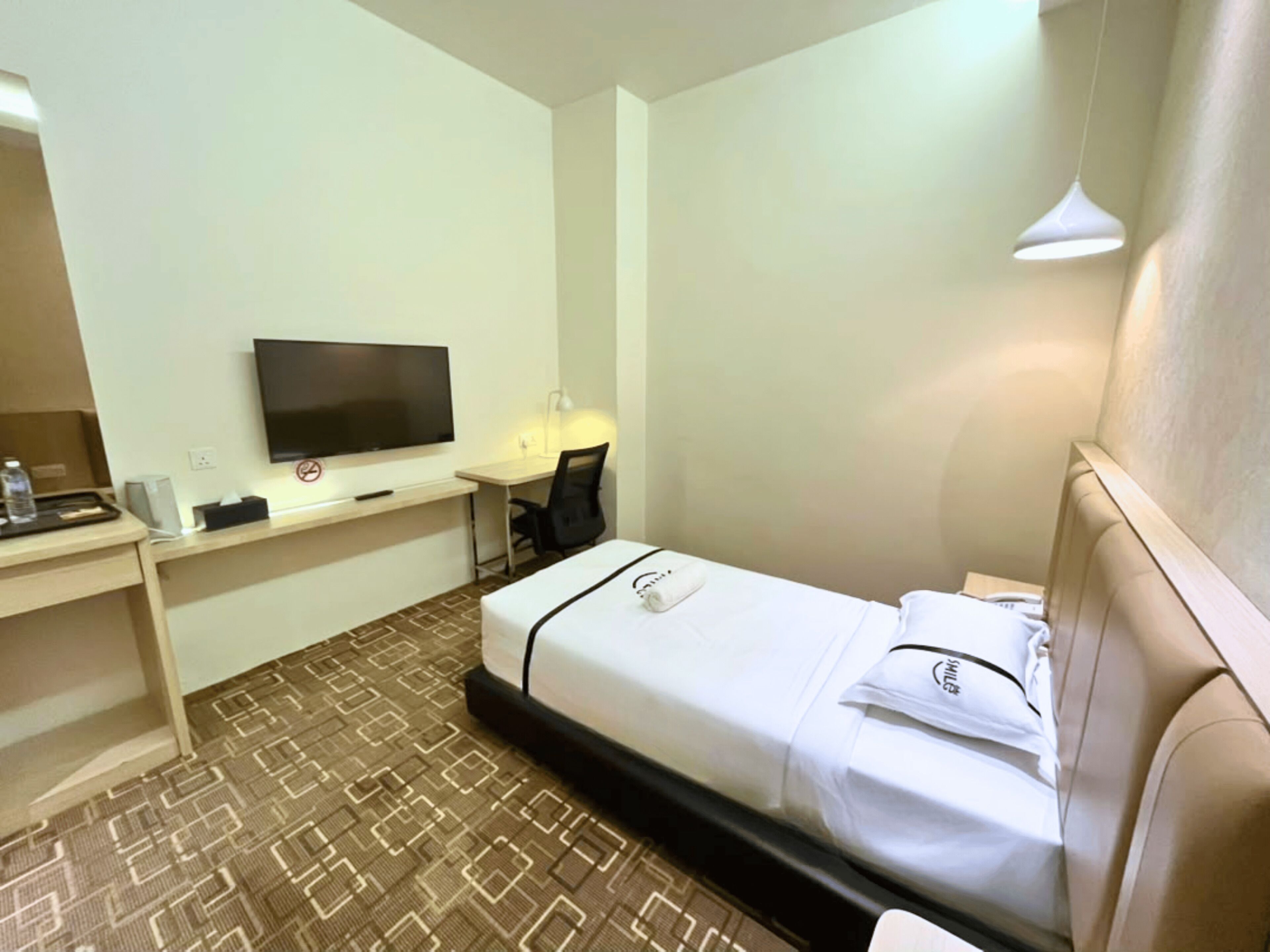 A hotel room with a bed, a desk with a flat-screen TV, a chair, and a lamp.