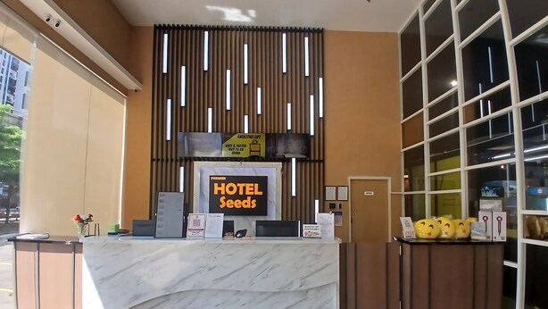 Un comptoir de réception d’hôtel avec un revêtement en marbre, une enseigne indiquant « HÔTEL SEEDS » et une autre, placée au-dessus, indiquant « ASCENSEUR POUR PERSONNES À MOBILITÉ RÉDUITE ».