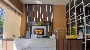 A hotel reception desk with a marble counter, a sign reading "HOTEL SEEDS", and a "FACILITIES LIFT" sign above.