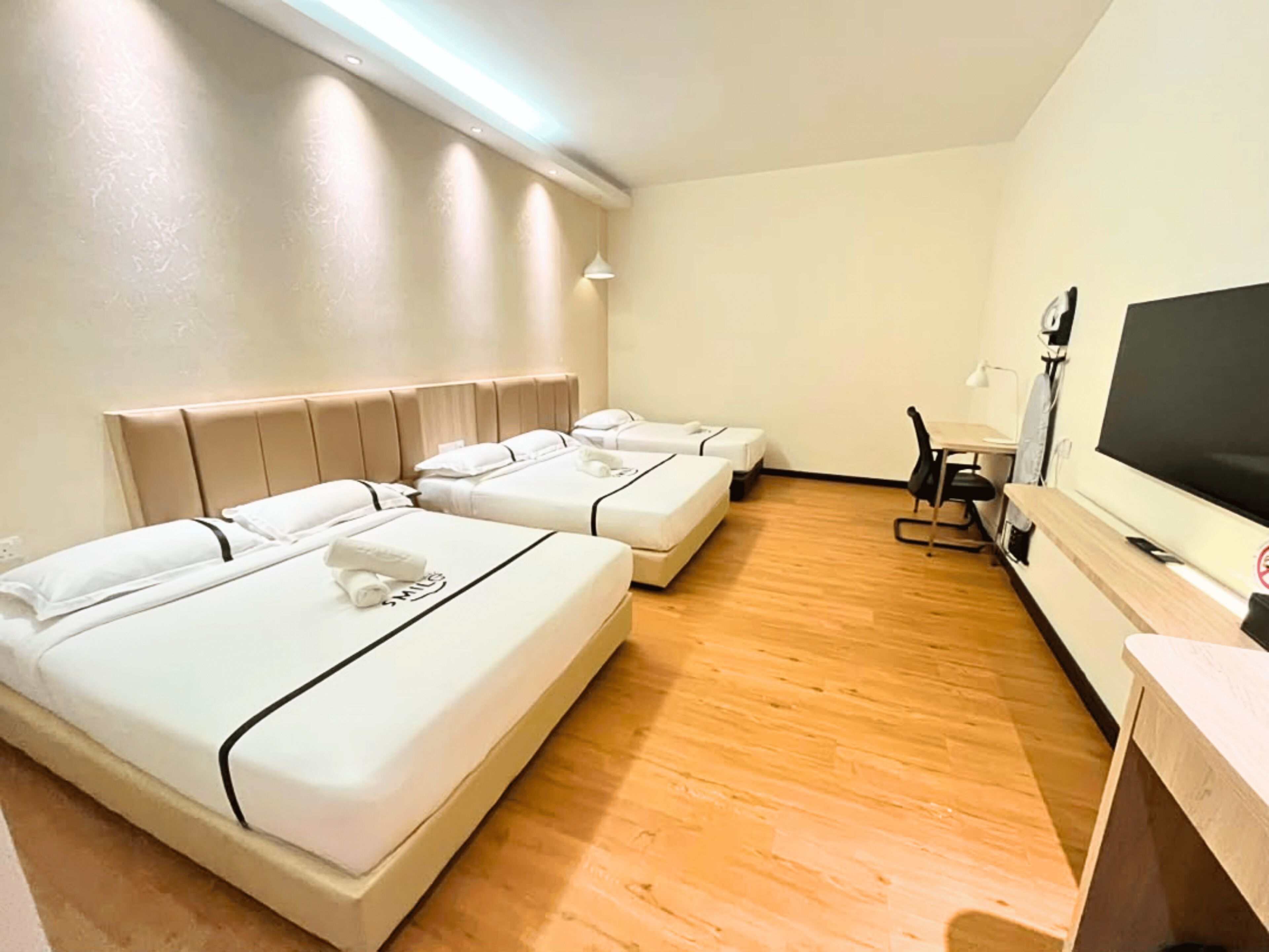 A hotel room with three beds, a desk, and a television.